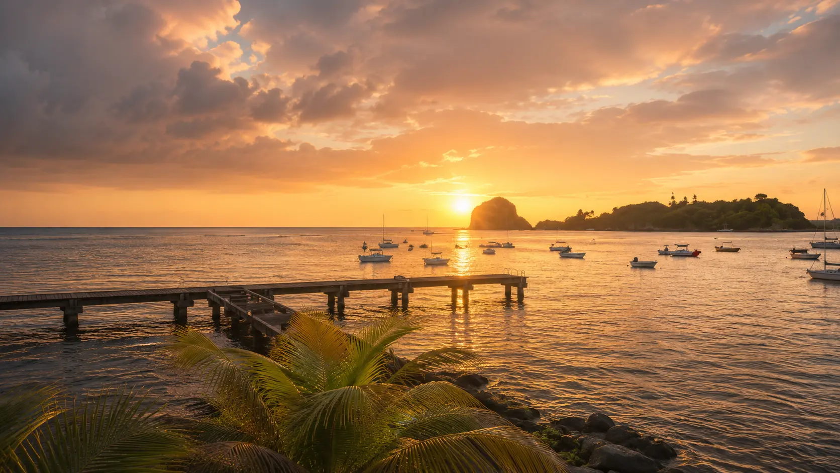 Golden sunset over Calliaqua Bay at Point Bay Resort, with anchored boats, palm fronds and the Grenadines horizon