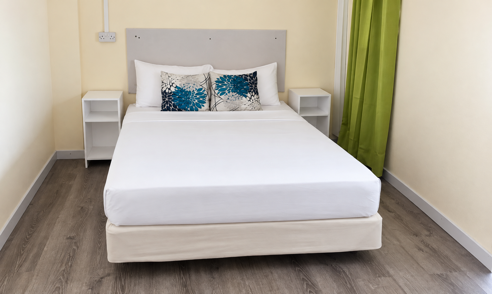 Ocean Front Junior Suite with a single queen bed, white linens and blue floral cushions, cream walls and a green curtain