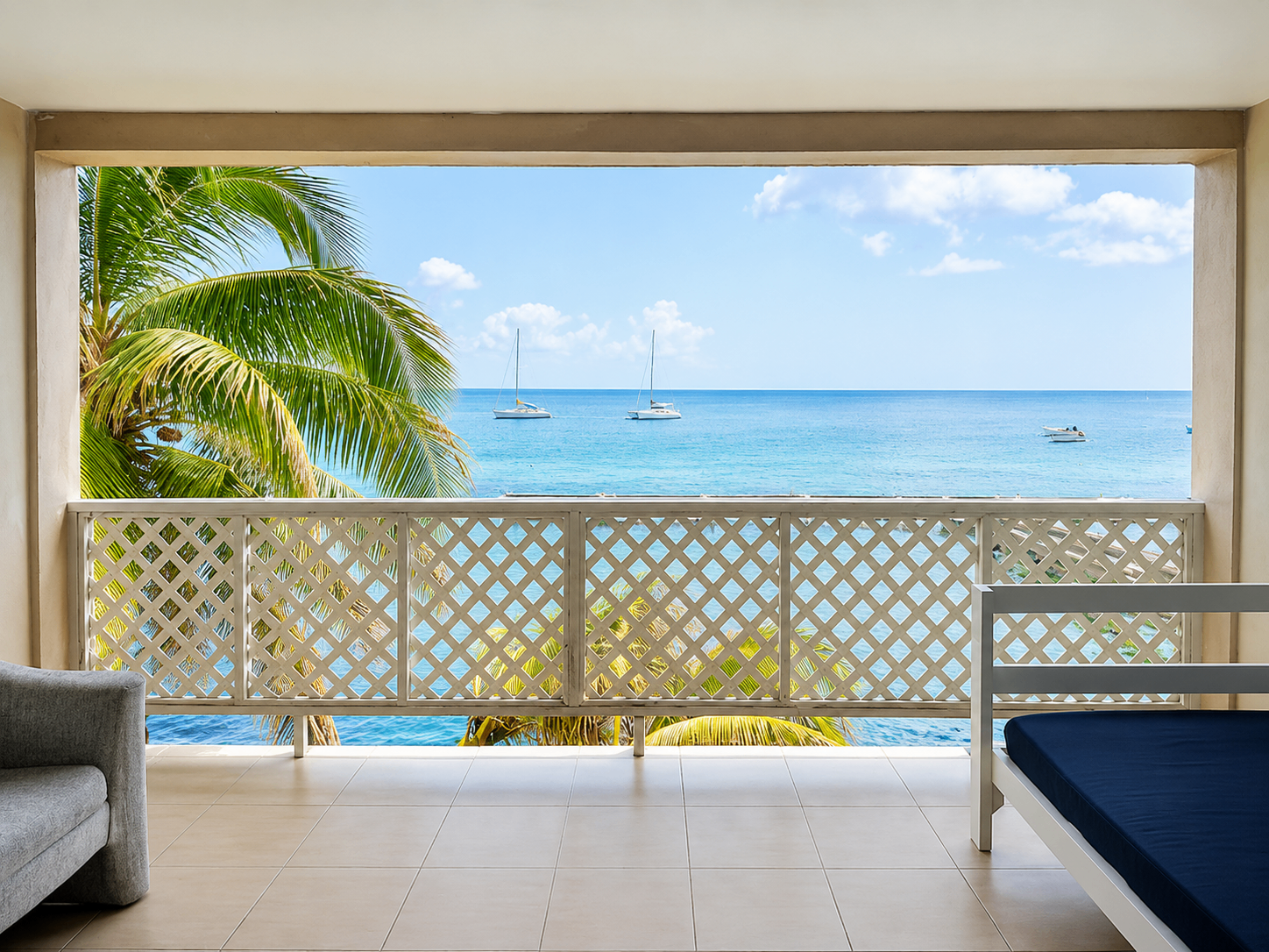 A balcony above the water with a lounge chair, palms and boats in the bay